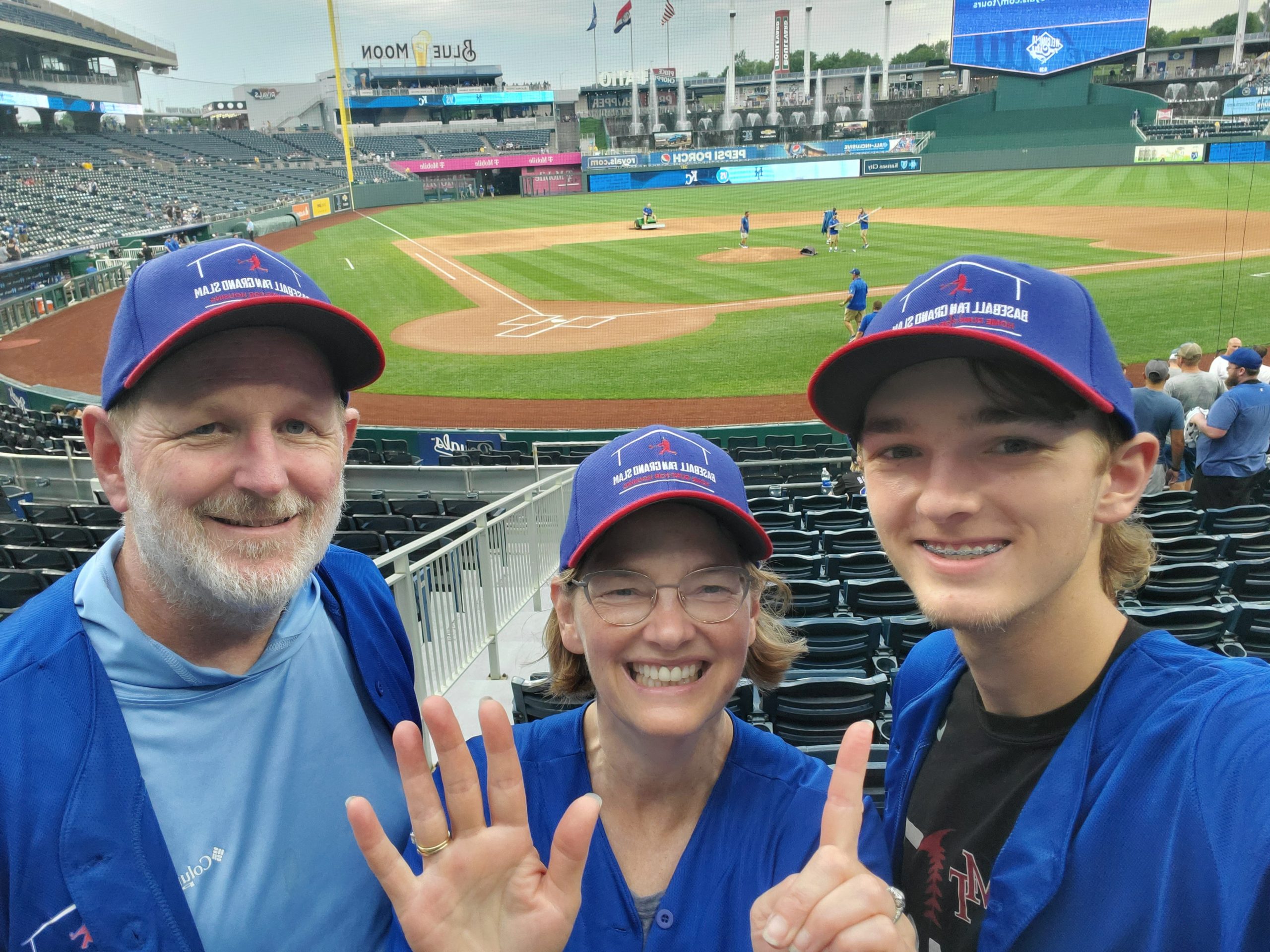 Photograph of Brad, Heather and Ryan from their seats at Kauffman Field, looking over the diamond and holding up 6 fingers for the sixth stadium they have seen!