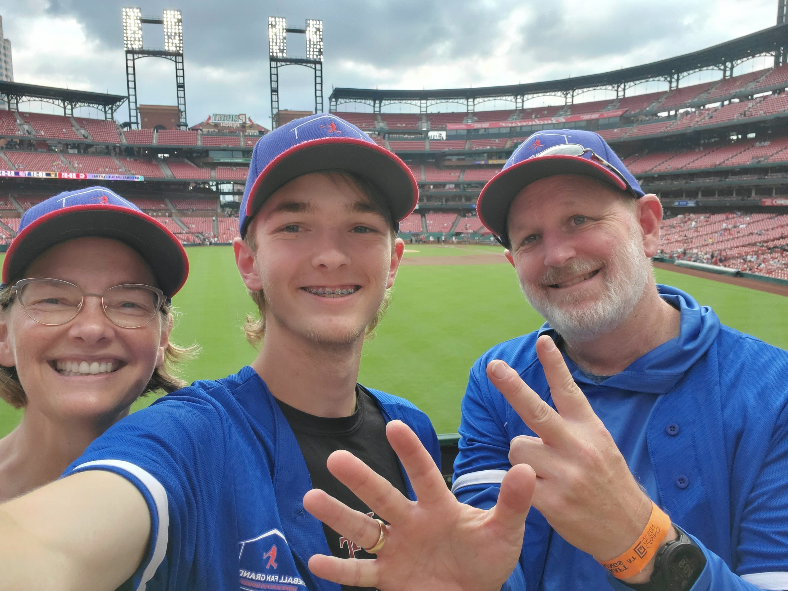 Heather, Ryan and Brad holding up 7 fingers to indicate the seventh stadium on their trip, in front of the diamond at Busch Stadium.