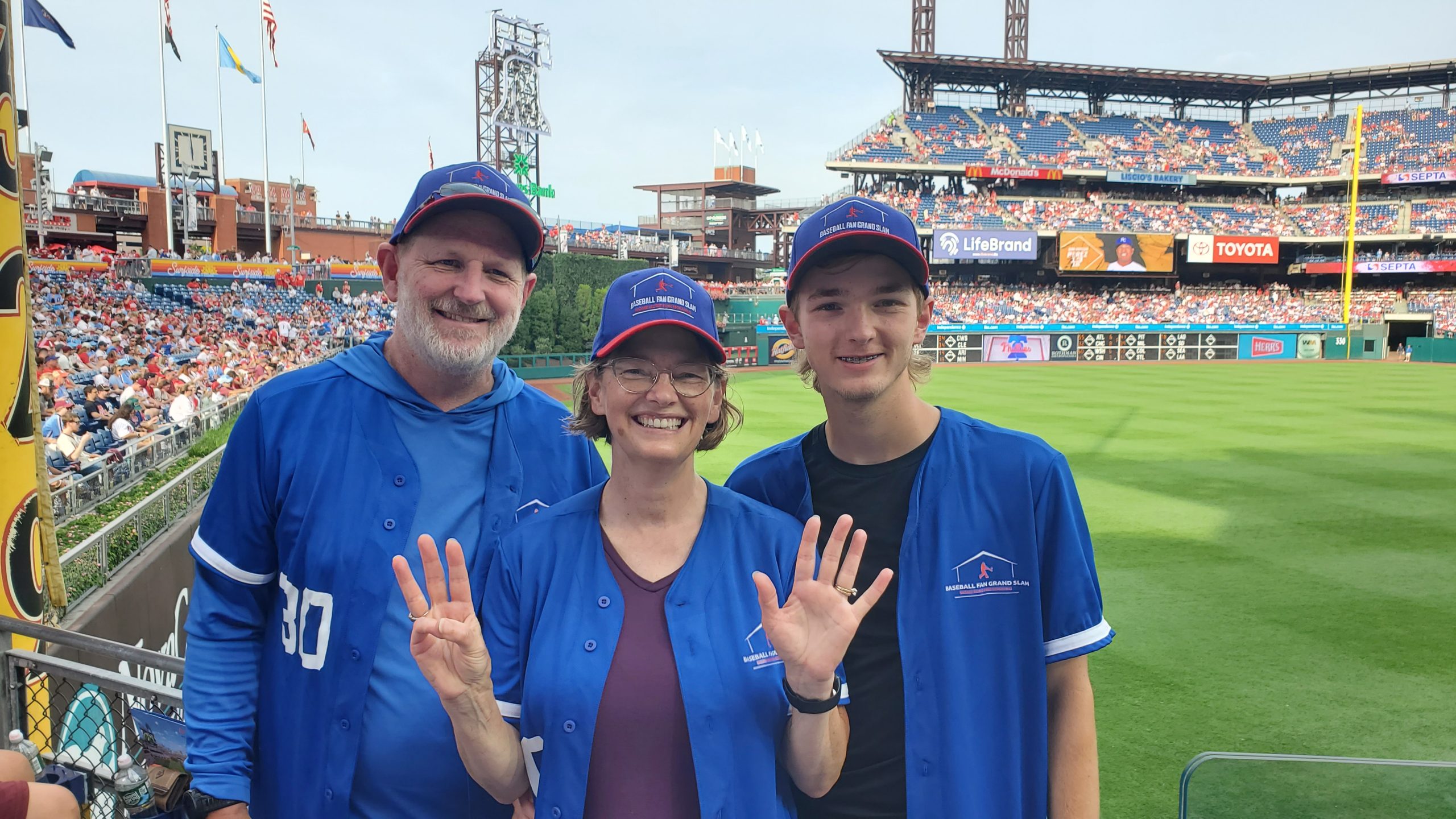 Brad, Heather and Ryan in Citizens Bank Park, with the baseball diamond behind them, holding up 8 fingers.